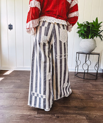 Wide leg cotton oversized gray and white striped pants with elastic back, button and zipper closure and crochet patch detail throughout.
