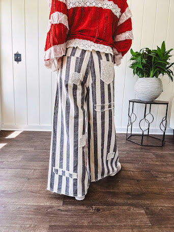Wide leg cotton oversized gray and white striped pants with elastic back, button and zipper closure and crochet patch detail throughout.