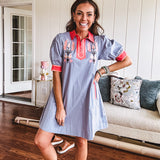 Slate blue dress with puffed, cuffed short sleeves, pockets, a contrasting coral collar and V neck, cuffs and trim and coral and pink embroidery at the yoke.