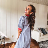 Slate blue dress with puffed, cuffed short sleeves, pockets, a contrasting coral collar and V neck, cuffs and trim and coral and pink embroidery at the yoke.