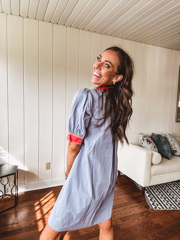 Slate blue dress with puffed, cuffed short sleeves, pockets, a contrasting coral collar and V neck, cuffs and trim and coral and pink embroidery at the yoke.