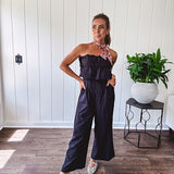 Fully lined black jumpsuit with sleeveless, ruffled bodice, smocked back, wide leg design and pockets at the pleated front.
