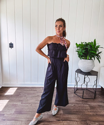 Fully lined black jumpsuit with sleeveless, ruffled bodice, smocked back, wide leg design and pockets at the pleated front.