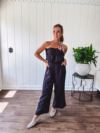 Fully lined black jumpsuit with sleeveless, ruffled bodice, smocked back, wide leg design and pockets at the pleated front.