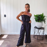 Fully lined black jumpsuit with sleeveless, ruffled bodice, smocked back, wide leg design and pockets at the pleated front.
