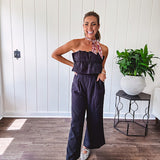 Fully lined black jumpsuit with sleeveless, ruffled bodice, smocked back, wide leg design and pockets at the pleated front.