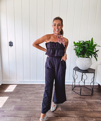 Fully lined black jumpsuit with sleeveless, ruffled bodice, smocked back, wide leg design and pockets at the pleated front.