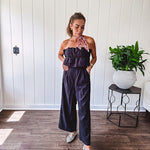 Fully lined black jumpsuit with sleeveless, ruffled bodice, smocked back, wide leg design and pockets at the pleated front.
