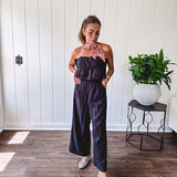 Fully lined black jumpsuit with sleeveless, ruffled bodice, smocked back, wide leg design and pockets at the pleated front.