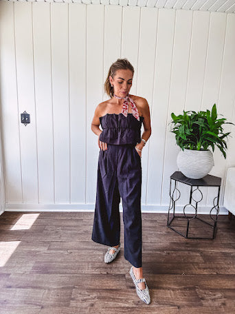 Fully lined black jumpsuit with sleeveless, ruffled bodice, smocked back, wide leg design and pockets at the pleated front.