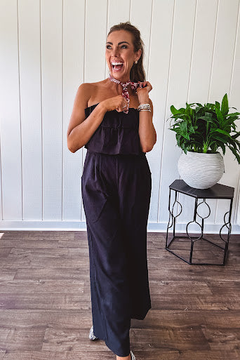 Fully lined black jumpsuit with sleeveless, ruffled bodice, smocked back, wide leg design and pockets at the pleated front.