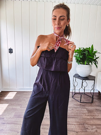 Fully lined black jumpsuit with sleeveless, ruffled bodice, smocked back, wide leg design and pockets at the pleated front.