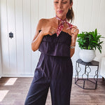 Fully lined black jumpsuit with sleeveless, ruffled bodice, smocked back, wide leg design and pockets at the pleated front.