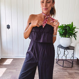 Fully lined black jumpsuit with sleeveless, ruffled bodice, smocked back, wide leg design and pockets at the pleated front.