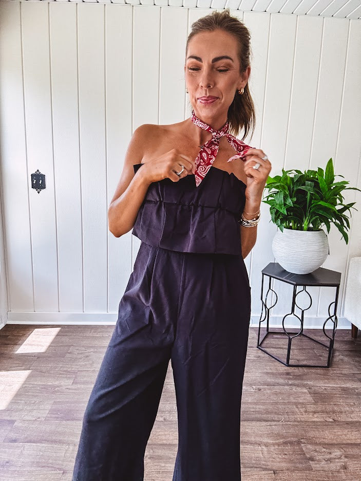 Fully lined black jumpsuit with sleeveless, ruffled bodice, smocked back, wide leg design and pockets at the pleated front.