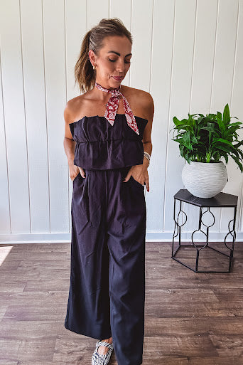 Fully lined black jumpsuit with sleeveless, ruffled bodice, smocked back, wide leg design and pockets at the pleated front.