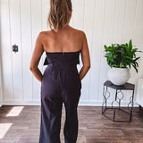 Fully lined black jumpsuit with sleeveless, ruffled bodice, smocked back, wide leg design and pockets at the pleated front.