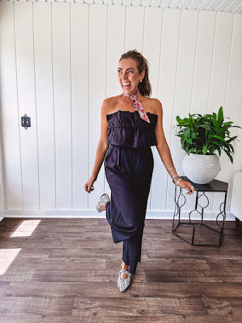 Fully lined black jumpsuit with sleeveless, ruffled bodice, smocked back, wide leg design and pockets at the pleated front.