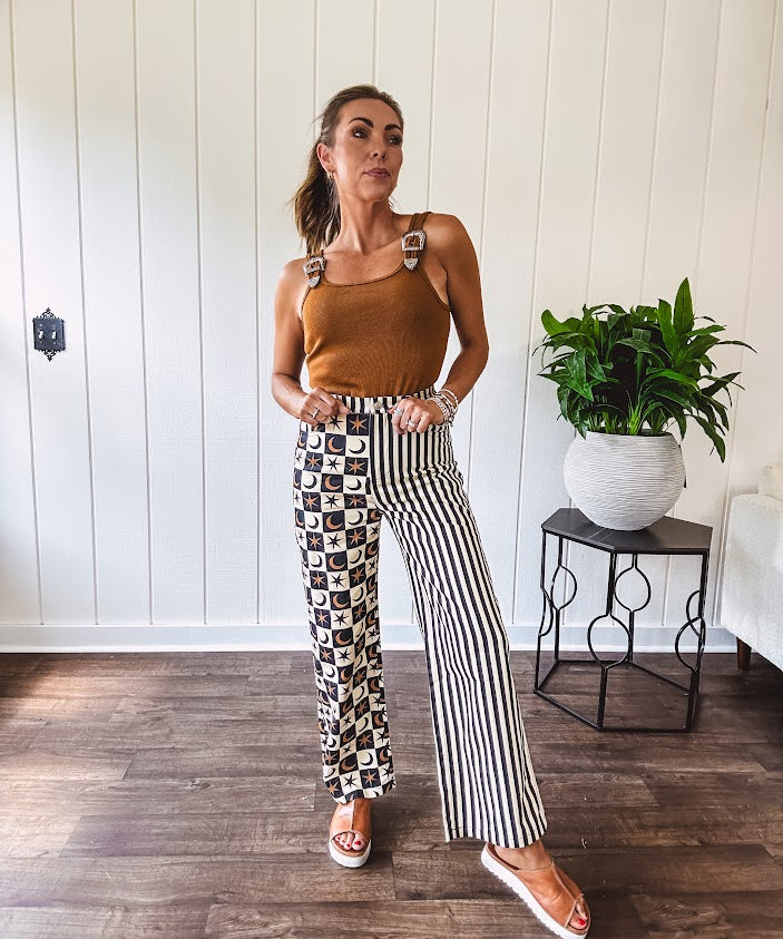 Wide leg lightweight button and zipper closure pants with elastic back waist featuring cream and black stripes down one leg and moon and star checkerboard in black, cream and mustard on the other leg.