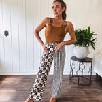 Wide leg lightweight button and zipper closure pants with elastic back waist featuring cream and black stripes down one leg and moon and star checkerboard in black, cream and mustard on the other leg.