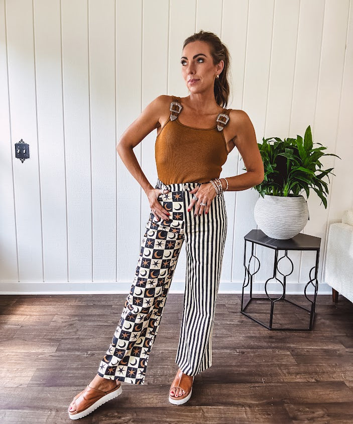Wide leg lightweight button and zipper closure pants with elastic back waist featuring cream and black stripes down one leg and moon and star checkerboard in black, cream and mustard on the other leg.
