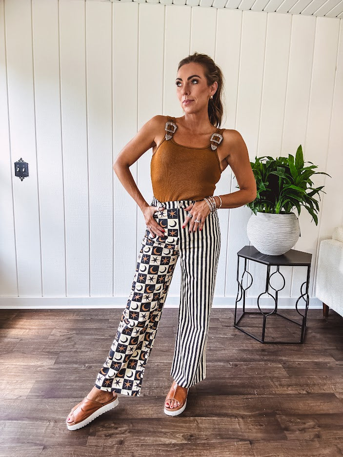 Wide leg lightweight button and zipper closure pants with elastic back waist featuring cream and black stripes down one leg and moon and star checkerboard in black, cream and mustard on the other leg.