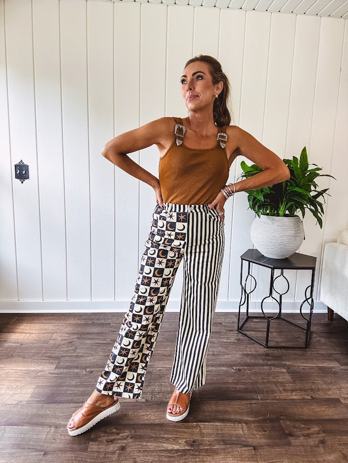 Wide leg lightweight button and zipper closure pants with elastic back waist featuring cream and black stripes down one leg and moon and star checkerboard in black, cream and mustard on the other leg.