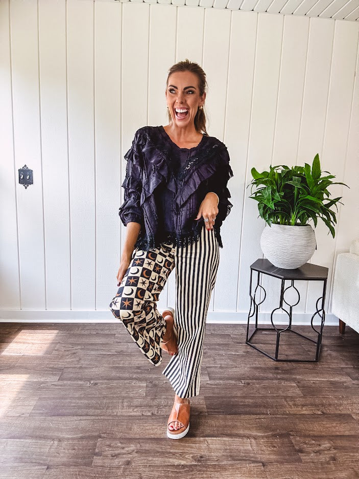 Wide leg lightweight button and zipper closure pants with elastic back waist featuring cream and black stripes down one leg and moon and star checkerboard in black, cream and mustard on the other leg.