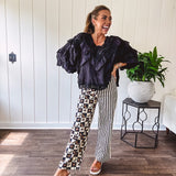Wide leg lightweight button and zipper closure pants with elastic back waist featuring cream and black stripes down one leg and moon and star checkerboard in black, cream and mustard on the other leg.
