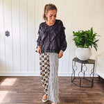 Wide leg lightweight button and zipper closure pants with elastic back waist featuring cream and black stripes down one leg and moon and star checkerboard in black, cream and mustard on the other leg.