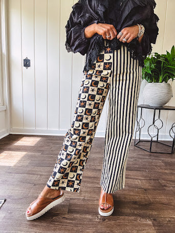 Wide leg lightweight button and zipper closure pants with elastic back waist featuring cream and black stripes down one leg and moon and star checkerboard in black, cream and mustard on the other leg.