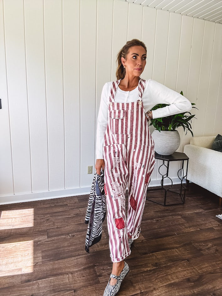 Cream and crimson striped overalls with button adjustable straps and sides with paint splatter and patchwork detail throughout.