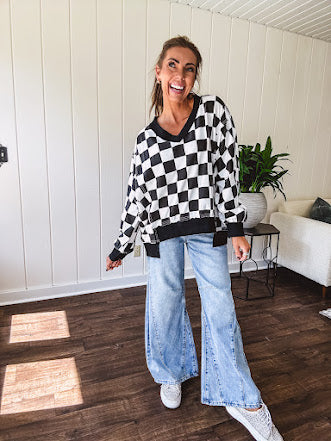 Lightweight black and white checkered long sleeve pullover with contrasting black V neck and cutout hem, with pockets.