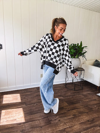 Lightweight black and white checkered long sleeve pullover with contrasting black V neck and cutout hem, with pockets.