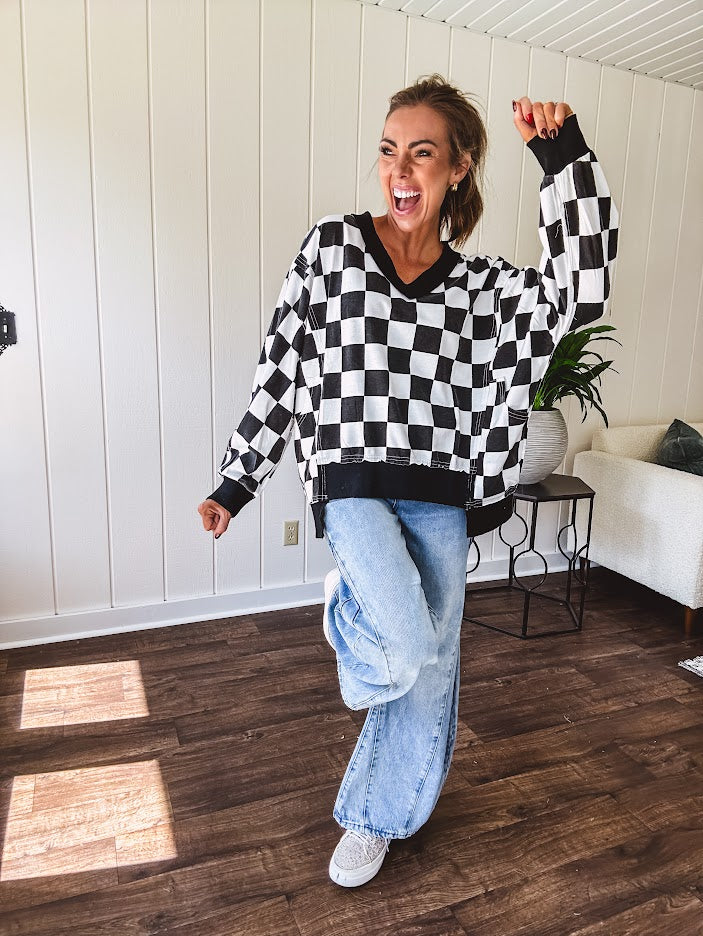 Lightweight black and white checkered long sleeve pullover with contrasting black V neck and cutout hem, with pockets.