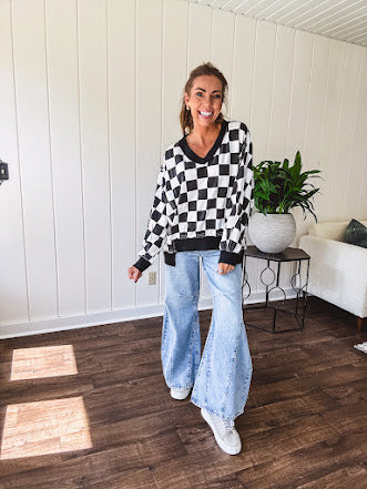 Lightweight black and white checkered long sleeve pullover with contrasting black V neck and cutout hem, with pockets.