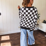 Lightweight black and white checkered long sleeve pullover with contrasting black V neck and cutout hem, with pockets.