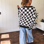 Lightweight black and white checkered long sleeve pullover with contrasting black V neck and cutout hem, with pockets.