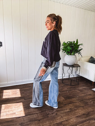 Wide leg medium washed denim pants featuring a washed black colorblock design on the outer legs and back pockets with exposed seams, bleach details and finished seams.