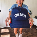 White canvas hat with black bill and black puff embroidered, backwards "Game Day" lettering on front.