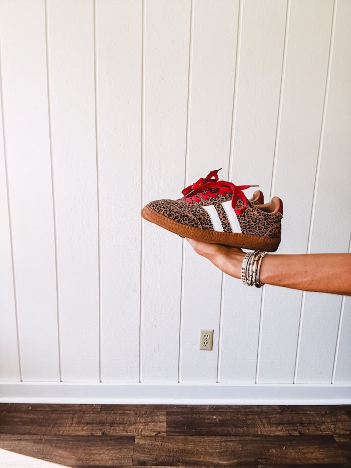 Mini leopard print sneakers with white stripes on the sides and contrasting red laces.