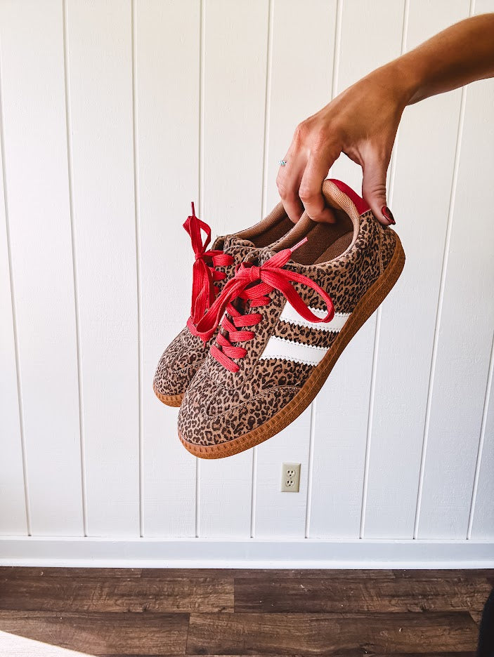 Mini leopard print sneakers with white stripes on the sides and contrasting red laces.