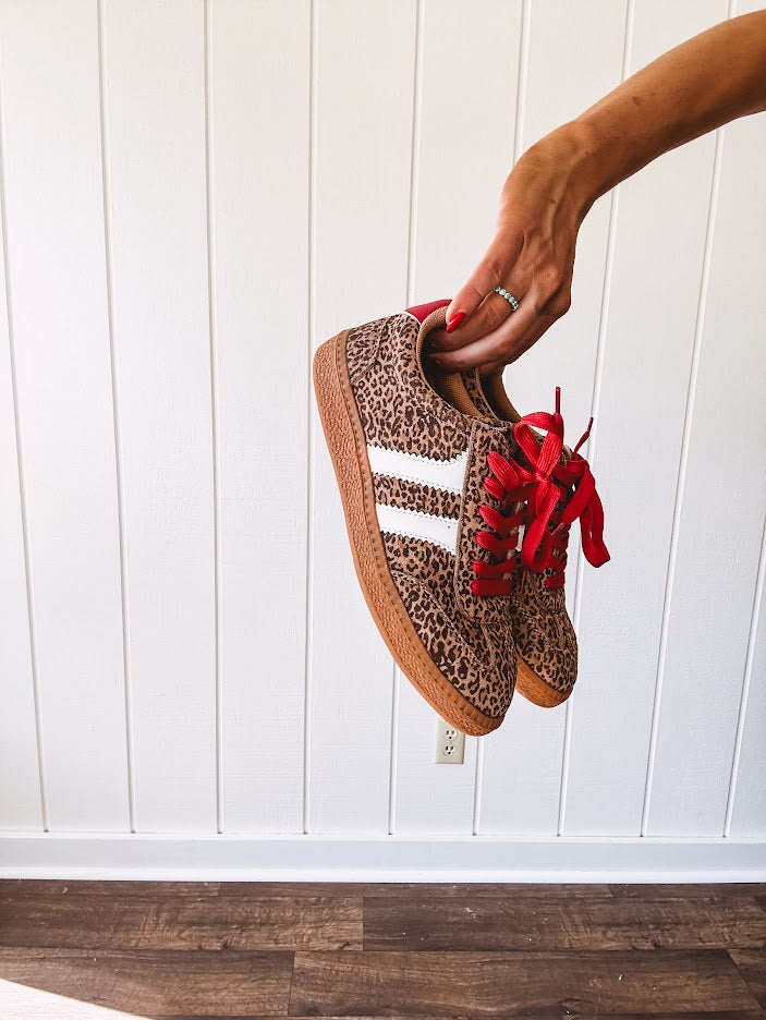 Mini leopard print sneakers with white stripes on the sides and contrasting red laces.