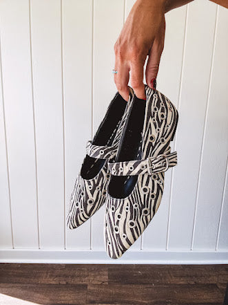 Cream and black zebra print ballet flat with pointed tow, Mary Jane style buckle across the top and silver rivet holes throughout.