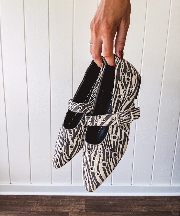 Cream and black zebra print ballet flat with pointed tow, Mary Jane style buckle across the top and silver rivet holes throughout.