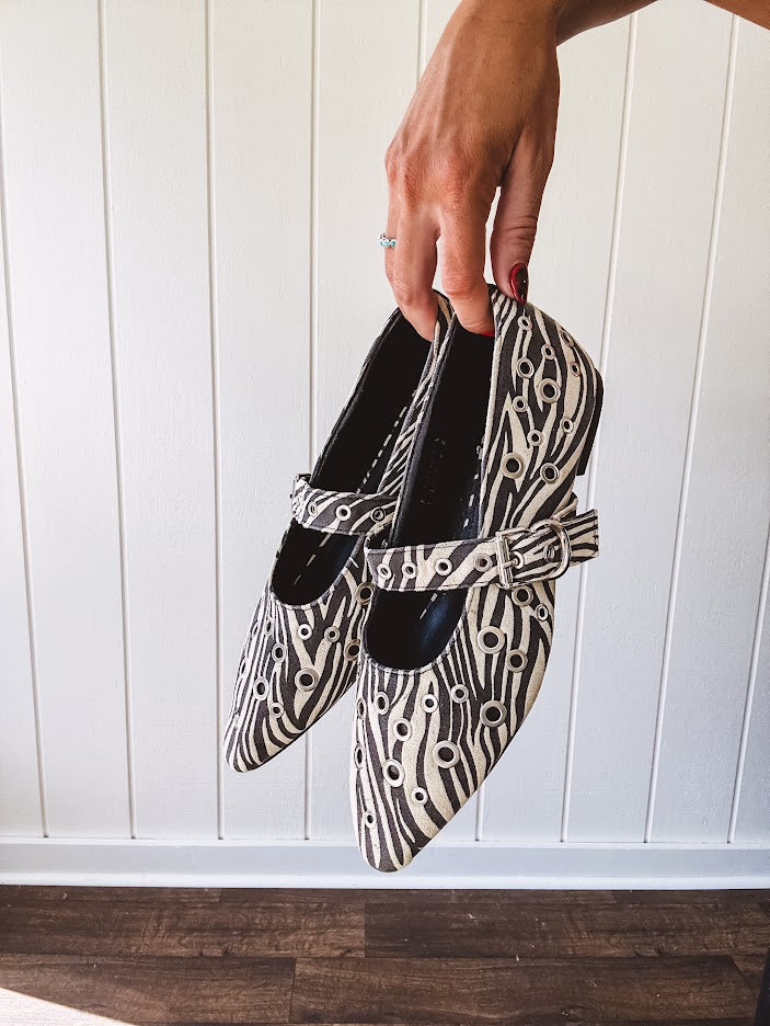 Cream and black zebra print ballet flat with pointed tow, Mary Jane style buckle across the top and silver rivet holes throughout.