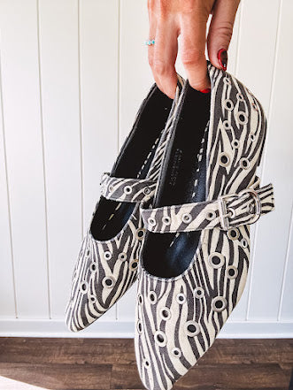Cream and black zebra print ballet flat with pointed tow, Mary Jane style buckle across the top and silver rivet holes throughout.