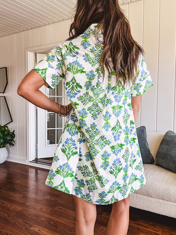 Cream shirt dress with blue and green floral print throughout, contrasting blue trim at the covered placket and hem, cuffed sleeves, mini length, fully lined.