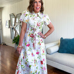 Crisp white button down shirt dress with collar, puffed short sleeves, matching belt and lined skirt featuring spring floral print.