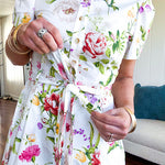 Crisp white button down shirt dress with collar, puffed short sleeves, matching belt and lined skirt featuring spring floral print.